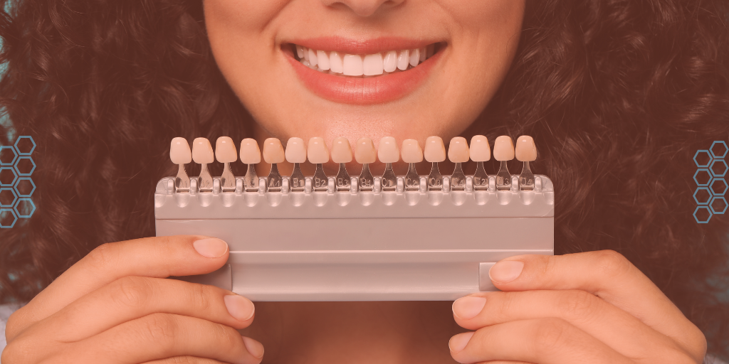 Woman smiling behind a tooth shade guide used to match porcelain veneer color