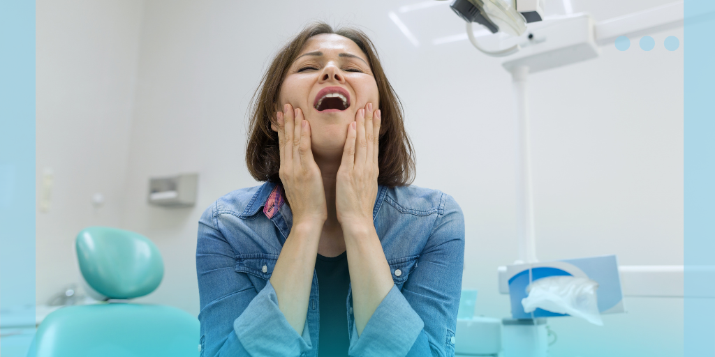 Woman holding her jaw in pain while sitting in a dental chair