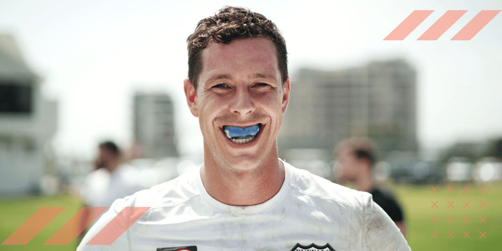 Athlete in a white jersey smiling with a blue sport mouthguard on a sports field